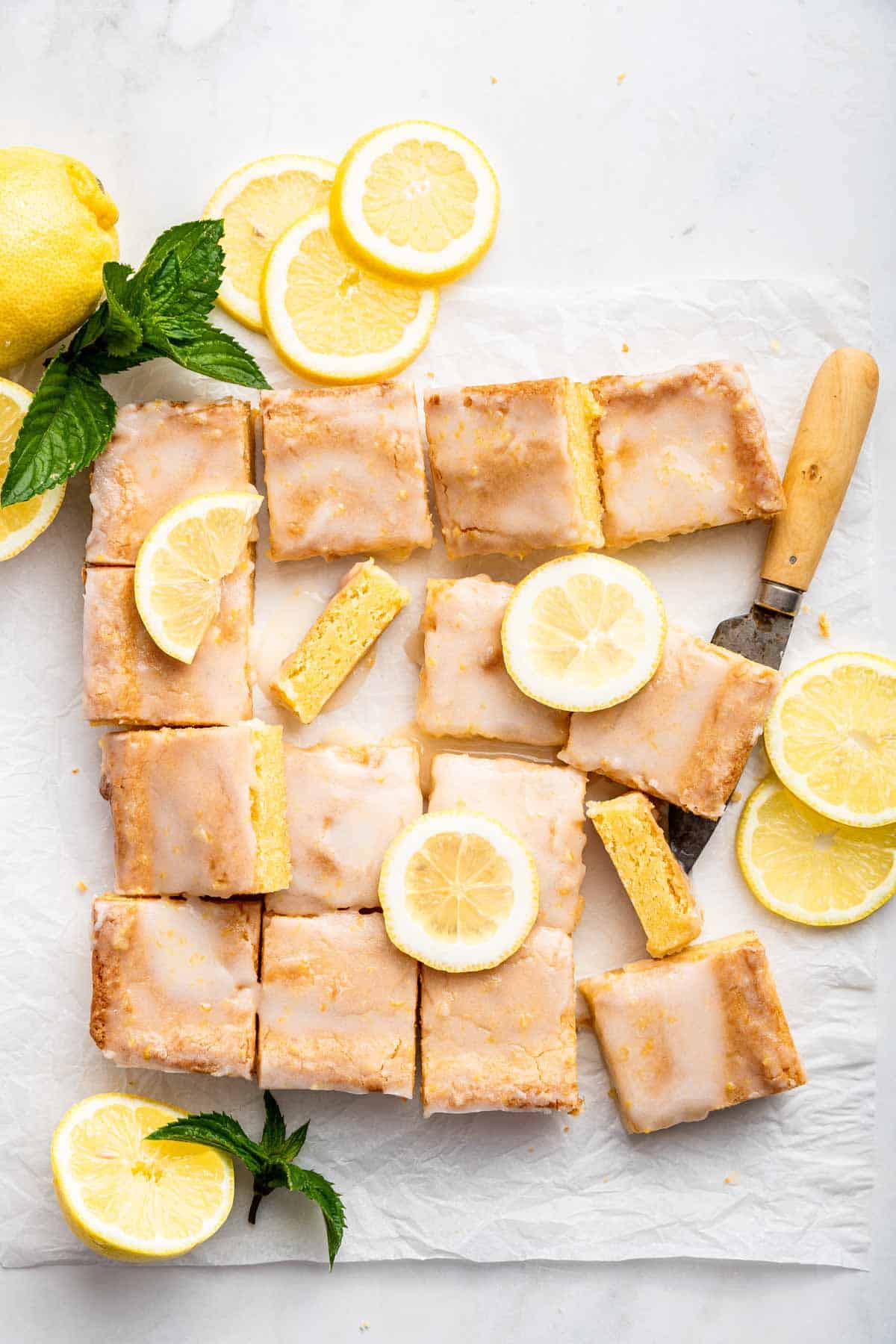 A square tray of lemon brownies cut into 16 pieces, decorated with lemon slices.